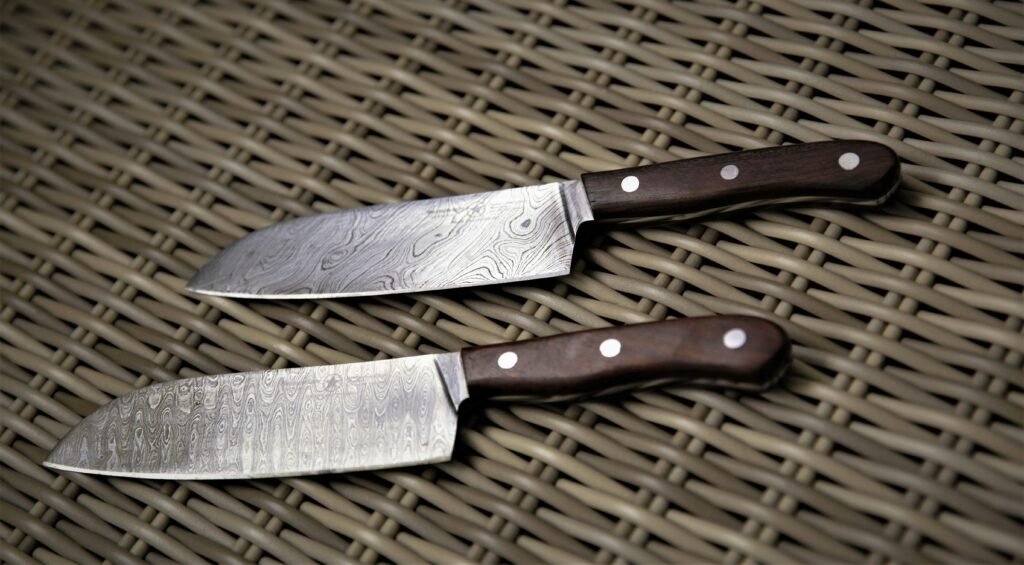 Close-up of two Damascus steel kitchen knives with wooden handles on a woven basket surface.